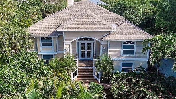 A two-story house with a central entrance, surrounded by lush greenery. - Sanibel Surfsound Home - Heated pool and easy walk to the beach (Sanibel)