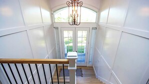 A staircase with wooden steps and a white railing, leading to a door with glass panels and a view of a garden. - Sanibel Surfsound Home - Heated pool and easy walk to the beach (Sanibel)