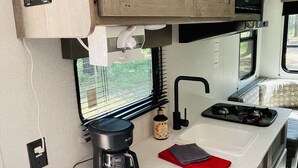 A compact kitchenette with wooden cabinets, a microwave, a coffee maker, and a sink. - Gennesis RV is located in Lost Pines Near Bastrop Lake (Bastrop)