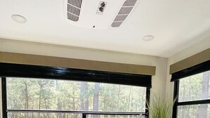 A cozy RV interior with a table and bench seating area, large windows offering a forest view, and a potted plant on the windowsill. - Gennesis RV is located in Lost Pines Near Bastrop Lake (Bastrop)