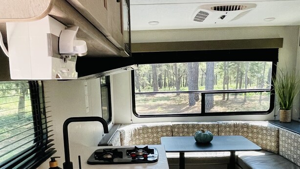 A compact RV kitchen with a stove, sink, and a window overlooking a forest. - Gennesis RV is located in Lost Pines Near Bastrop Lake (Bastrop)