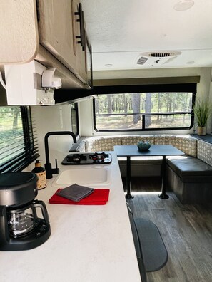 A compact RV kitchen with a stove, sink, and a window overlooking a forest. - Gennesis RV is located in Lost Pines Near Bastrop Lake (Bastrop)