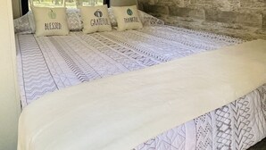 A bedroom with a large bed, a stone wall, and a window with a view of trees. - Gennesis RV is located in Lost Pines Near Bastrop Lake (Bastrop)