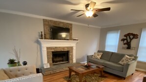 A living room with a fireplace, a sofa, a coffee table, and a ceiling fan. - Beautiful House 4 ENTIRE Family near Suntrust Park (Marietta)