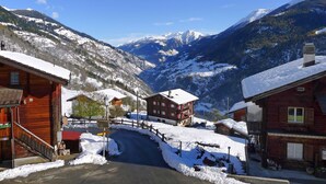 Un pueblo de montaña con edificios de madera, una carretera cubierta de nieve y vistas a montañas nevadas.