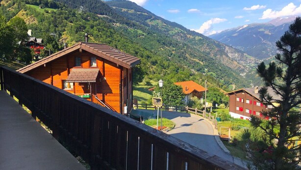 Una cabaña de madera con techo inclinado, un balcón y vistas a un paisaje montañoso.
