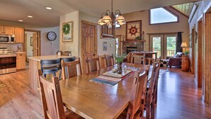 A spacious kitchen with wooden cabinets, a dining area with a large wooden table, and a cozy living room with a fireplace. - Idyllic Hill City Home - Hike, Bike & ATV! (Hill City)