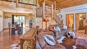 A spacious living area with a wooden staircase, a dining table with chairs, a sofa set, and a cowhide rug. - Idyllic Hill City Home - Hike, Bike & ATV! (Hill City)