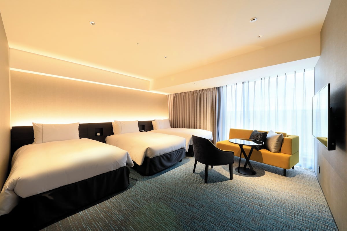 A hotel room with two beds, a sofa, a small table, and a TV mounted on the wall.