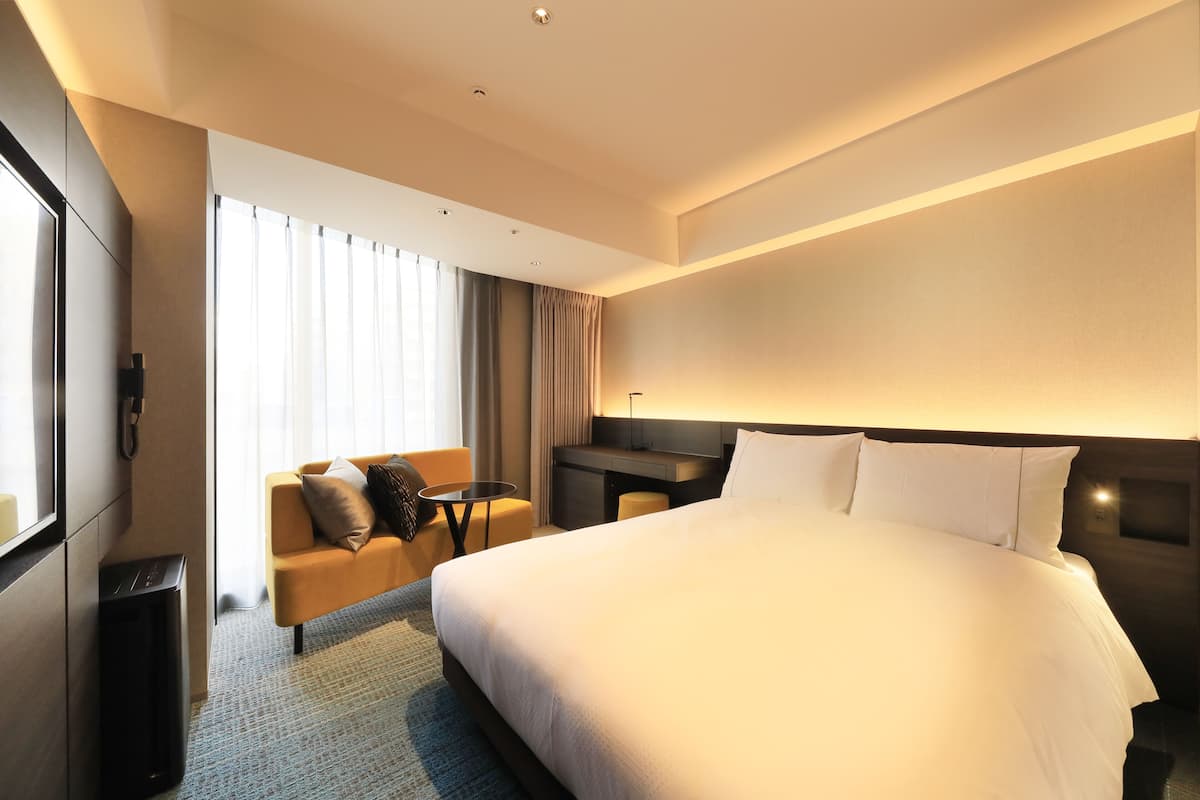 A hotel room with a large bed, a sofa, a desk, and a trash bin.