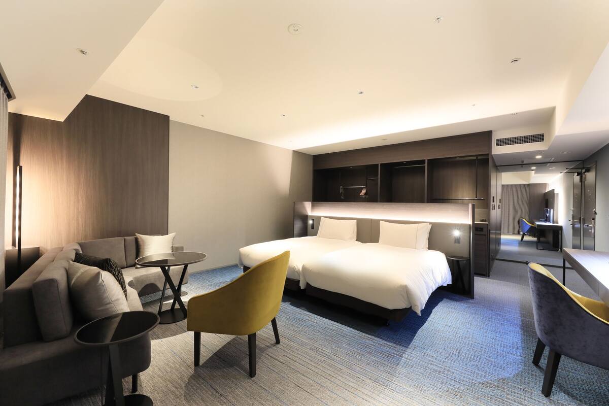 A modern hotel room with a large bed, a sofa, a small table, and a chair.