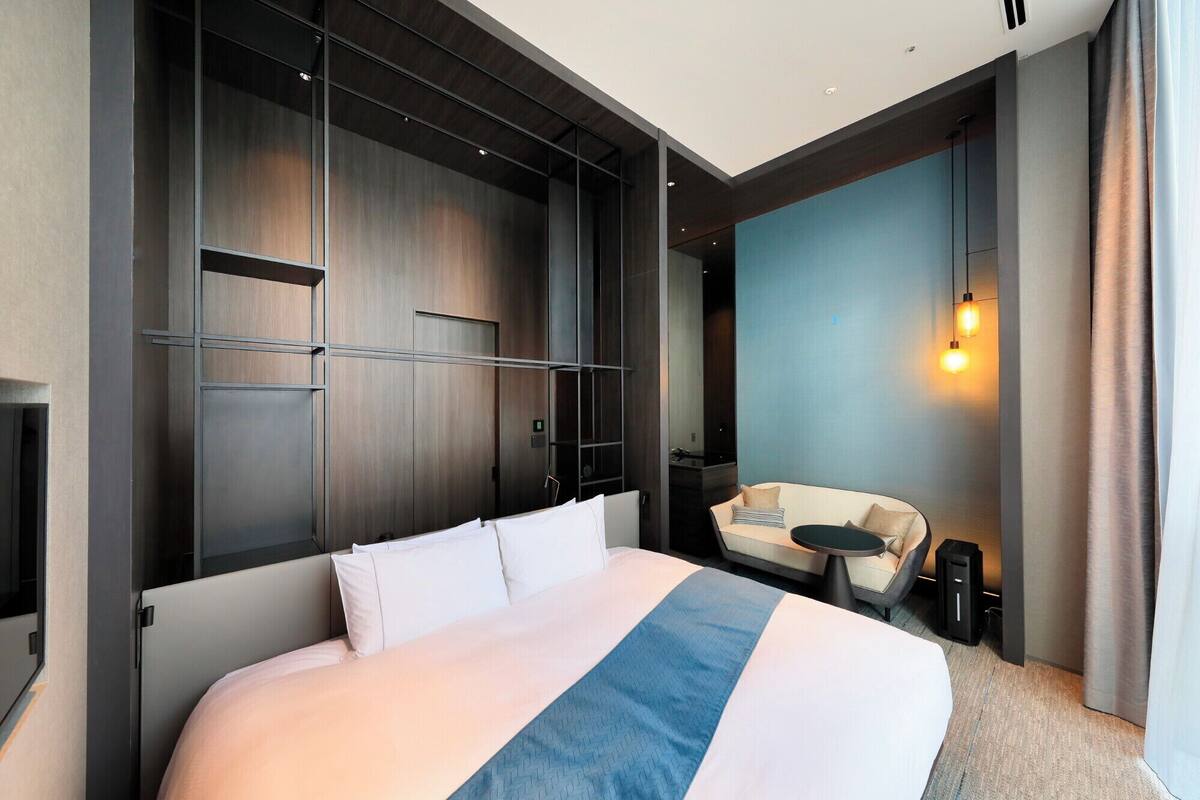 A modern hotel room with a large bed, a desk, and a seating area.