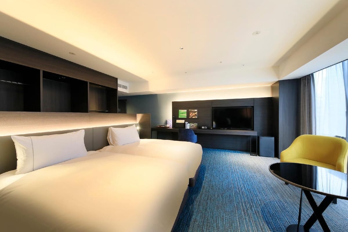 A hotel room with a large bed, a TV, a small table, and a chair.