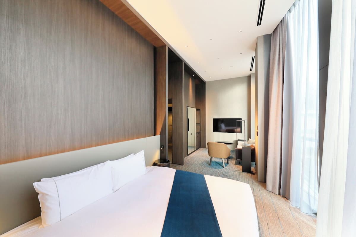 A hotel room with a large bed, a desk, a chair, a TV, and a wardrobe.