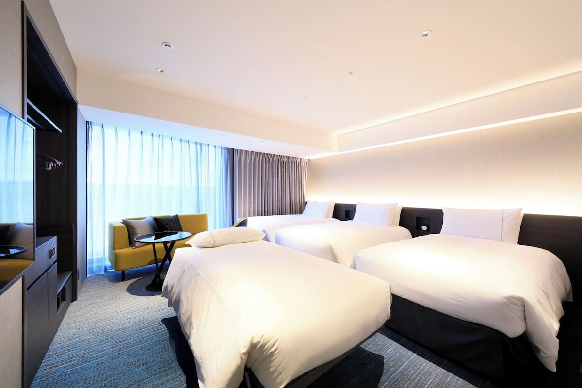 A hotel room with two beds, a sofa, a small table, and a TV.