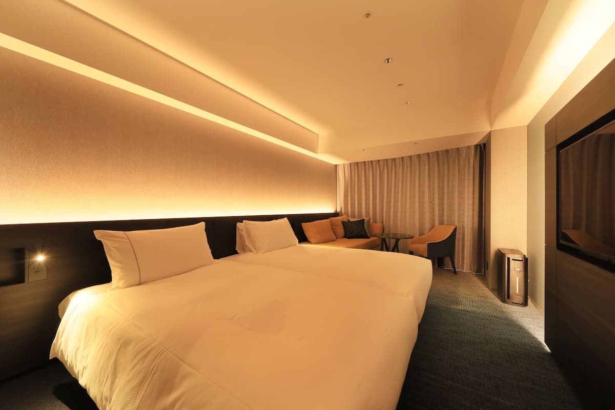 A modern hotel room with a large bed, a desk, and a chair.