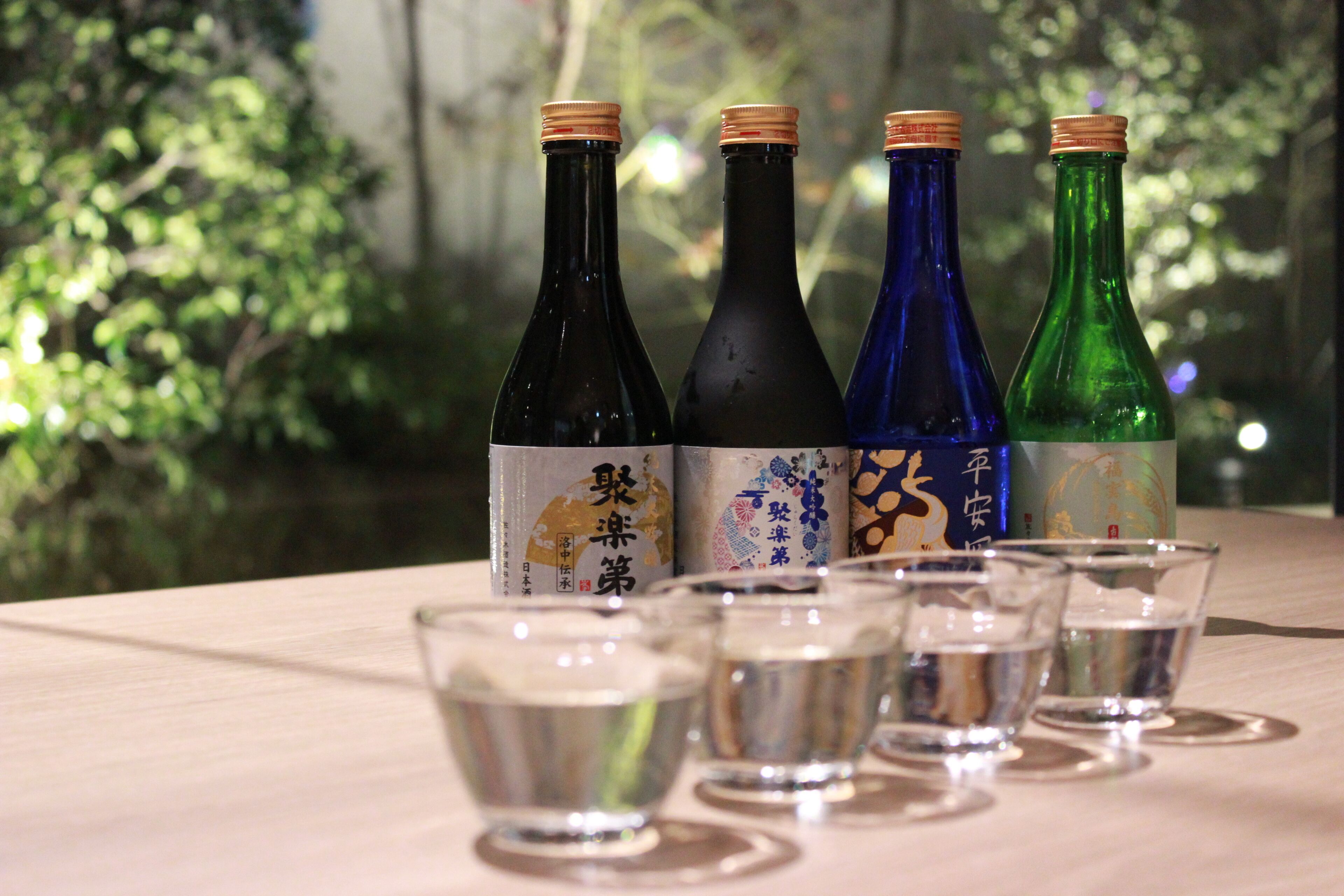 Four bottles of sake with labels, and five small glasses in front of them.