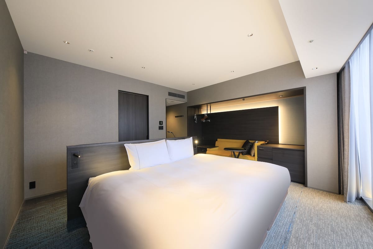 A modern hotel room with a large bed, a desk, and a built-in TV.