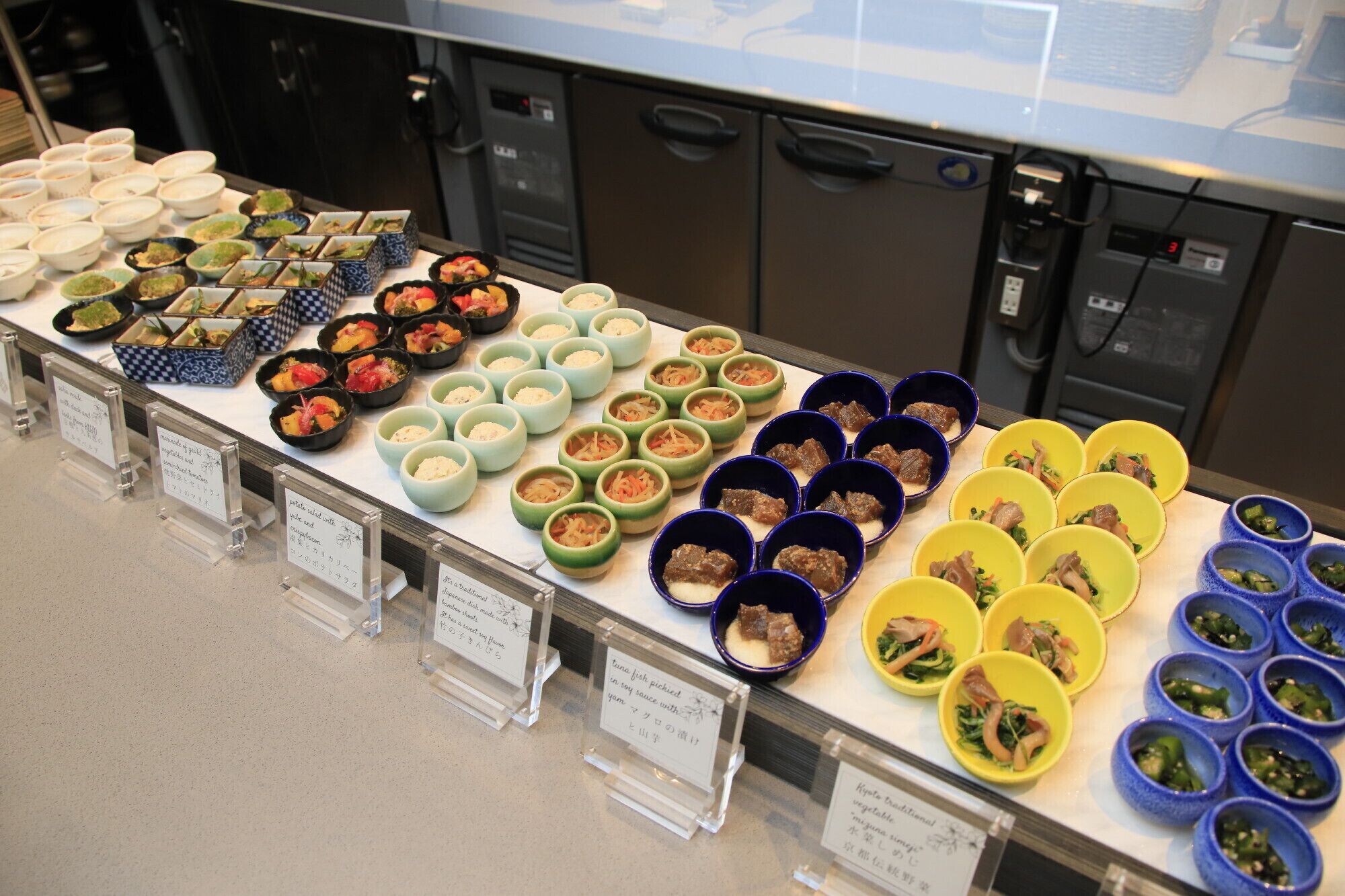 Un buffet proposant divers plats présentés dans des bols, disposés sur une table et accompagnés d’étiquettes explicatives.