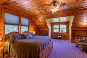 A cozy log cabin bedroom with a large bed, a desk, and a chair.