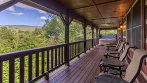 A covered porch with wooden railings, outdoor seating, and a view of a forested landscape. - Amen Corner - Close to Boone! Hot Tub, Pet Friendly, Ping Pong, Foosball, Mountain Views (Vilas)
