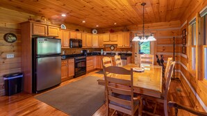 A wooden cabin interior with a kitchen, dining area, and a large window. - Amen Corner - Close to Boone! Hot Tub, Pet Friendly, Ping Pong, Foosball, Mountain Views (Vilas)