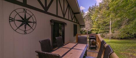An outdoor dining area with a wooden deck, a large table with chairs, and a compass wall decoration.