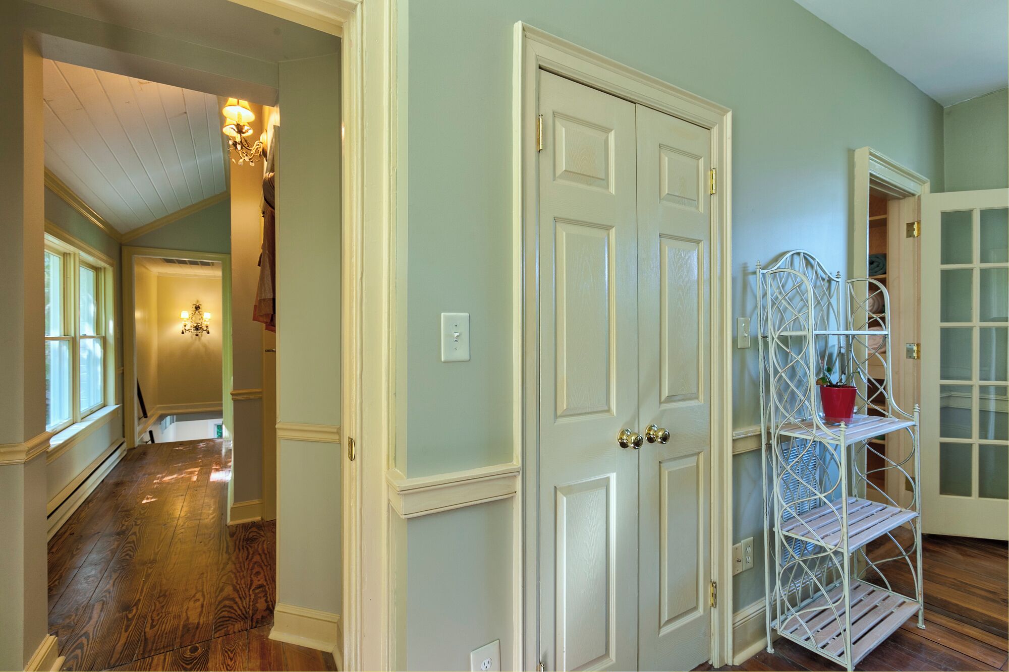 A hallway with wooden flooring, white doors, and a metal shelving unit with a red pot.