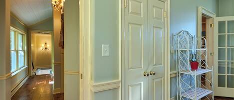 A hallway with wooden flooring, white doors, and a metal shelving unit with a red pot.
