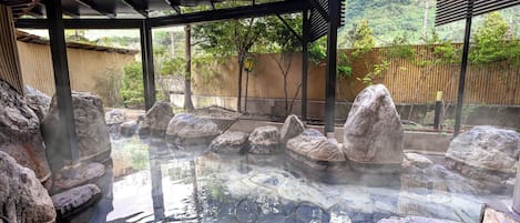 A hot spring area with stone flooring, large rocks, and a covered shelter.