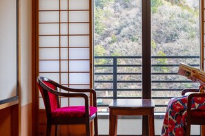 A traditional Japanese room with tatami flooring, a shoji screen, and a view of a mountainous landscape.