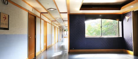 A long, narrow hallway with wooden doors and a large window at the end.