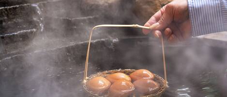 A hand holding a basket with eggs over a steaming water source.