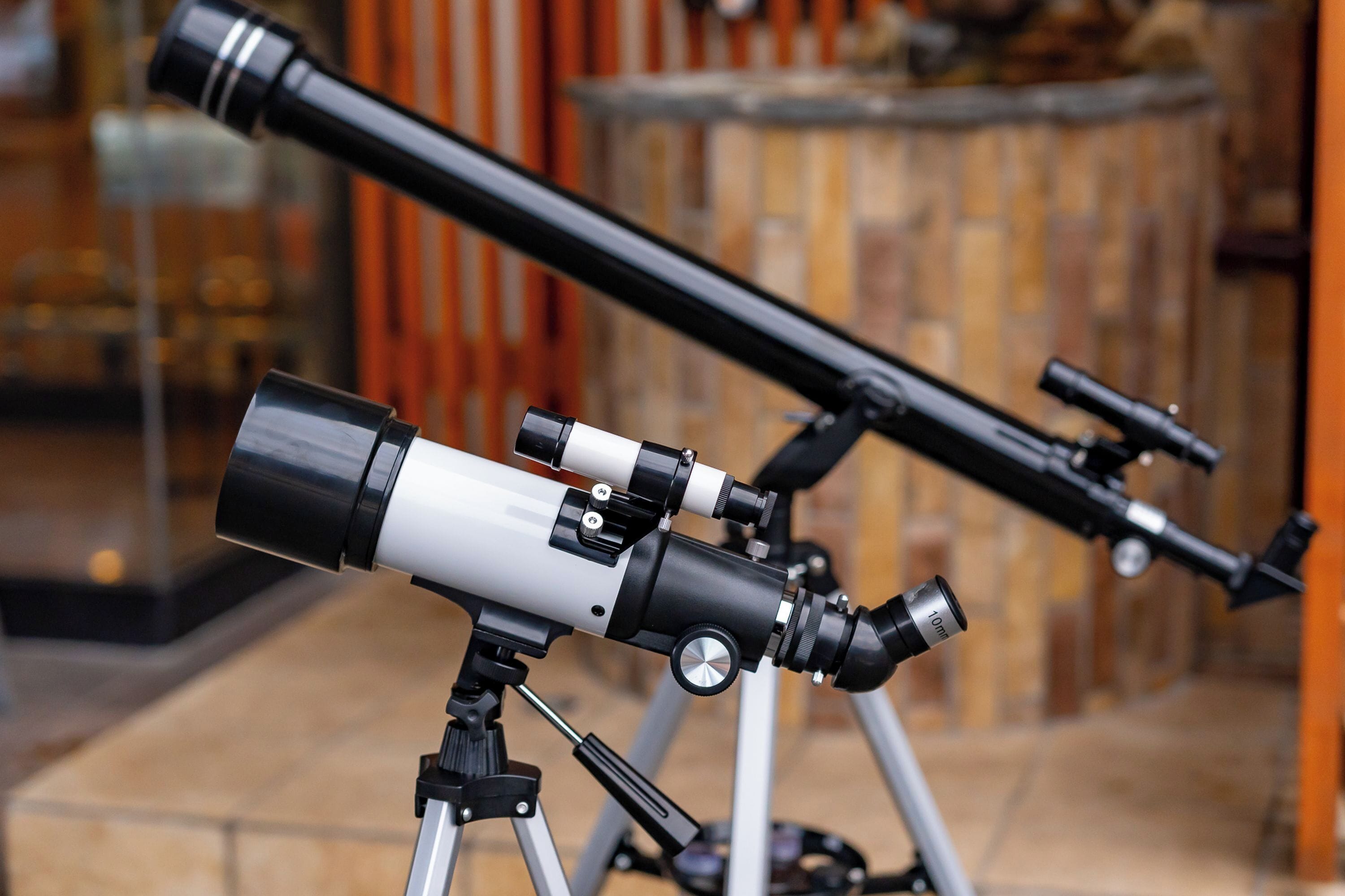 Telescopes on a tripod in a room with a tiled floor and a brick wall.