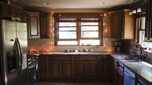 Een keuken met houten kastjes, een roestvrijstalen koelkast, een dubbele gootsteen en een raam met lichtslingers.