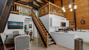 Een moderne keuken met witte kasten, een houten trap en een eethoek met een tafel en stoelen.