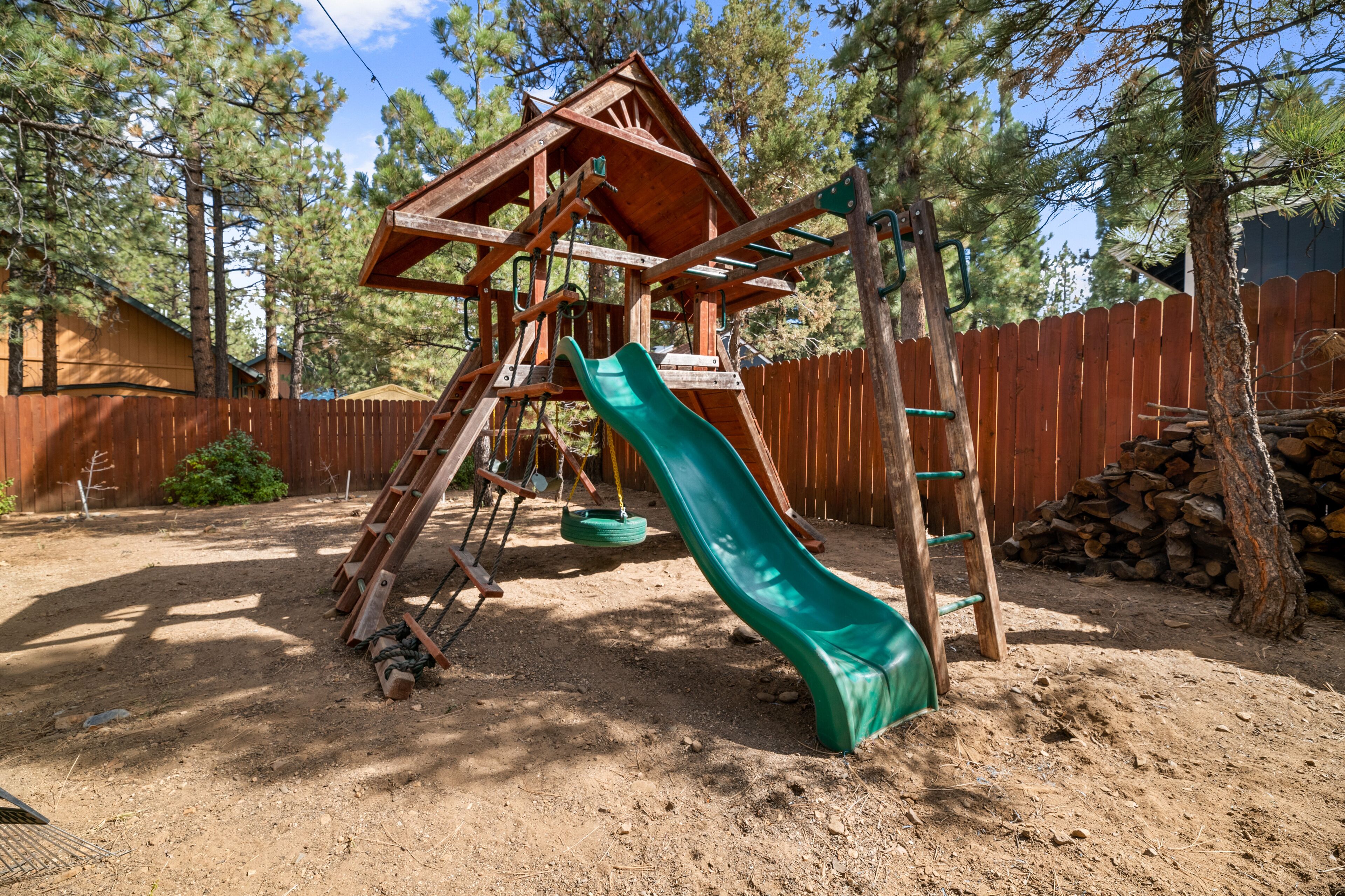A wooden play structure with a slide and swings in a backyard.