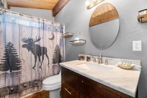 Un baño con cortina de ducha de madera, inodoro blanco, lavamanos de mármol y muebles de madera.