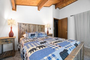 Un dormitorio con cabecera de madera, colcha a cuadros, dos mesitas de noche con lámparas y una puerta de madera.