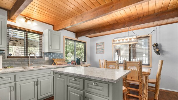 A kitchen with light gray cabinets, a granite countertop, wooden ceiling beams, and a dining area with a wooden table and chairs.