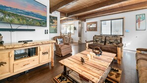 A spacious living room with wooden furniture, a large painting of a mountain landscape, and a cozy fireplace.