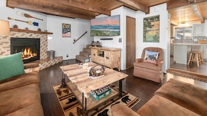 A cozy living room with a fireplace, wooden furniture, and a view of a mountain landscape.