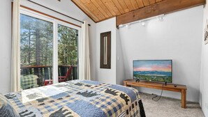 A bedroom with a large bed, a TV on a wooden stand, and a view of trees through a sliding door.