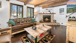 A cozy living room with a fireplace, wooden ceiling beams, a leather sofa, and a coffee table.