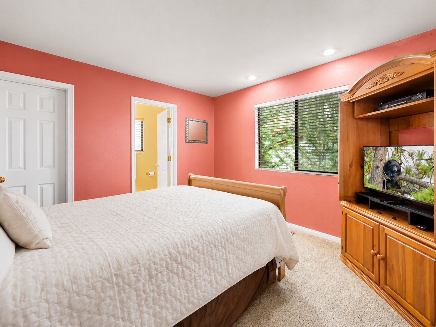 A bedroom with a bed, a television on a wooden cabinet, and a door leading to another room.