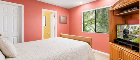 A bedroom with a bed, a television on a wooden cabinet, and a door leading to another room.