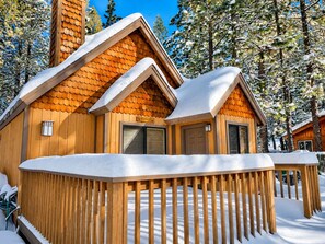 A wooden cabin with a snow-covered roof and a wooden deck.