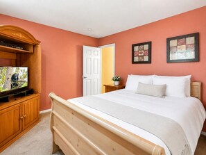 A bedroom with a bed, a television on a wooden cabinet, and two framed pictures on the wall.