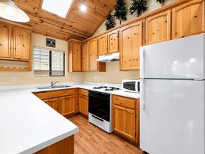 Une cuisine avec des meubles de rangement en bois, un plan de travail blanc, une cuisinière, un four à micro-ondes et un réfrigérateur.