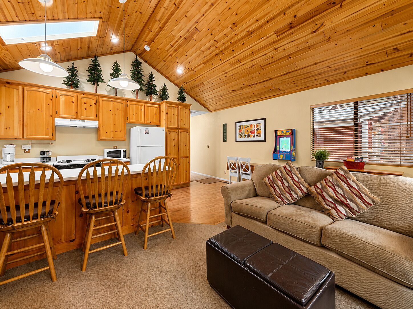 A cozy living area with a kitchen, wooden ceiling, and a sofa with patterned cushions.